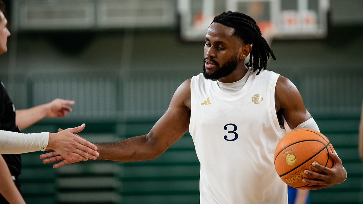 Joueur de basketball en tenue rouge BRVS n°3 tenant un ballon, debout devant un panneau d’affichage lumineux en salle.