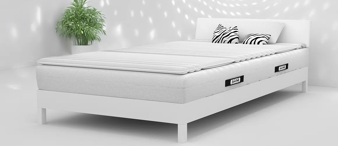 Surmatelas BODYGUARD® sur un lit blanc dans une chambre lumineuse à la décoration minimaliste.