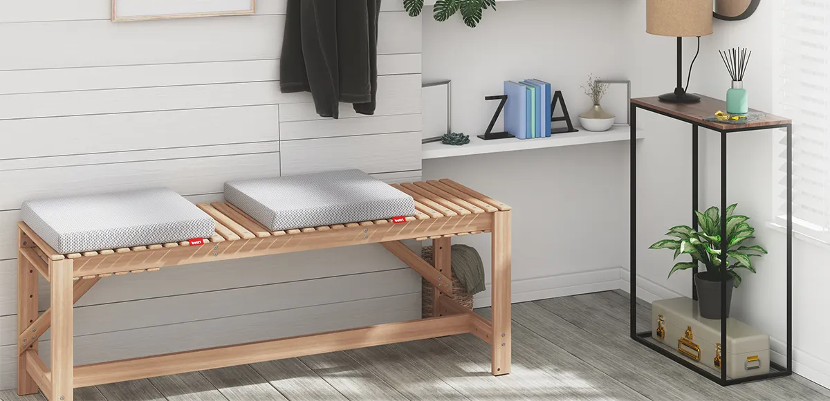 Deux coussins de chaise BODYGUARD® disposés sur un banc en bois dans une entrée. Le décor inclut une étagère blanche, des livres, une lampe et une plante verte.