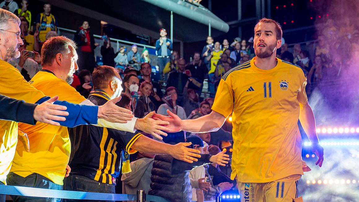 Foto: Ein ALBA Berlin Spieler beim Einlauf in die Halle, klatscht einige ihm entgegengestreckte Hände ab.