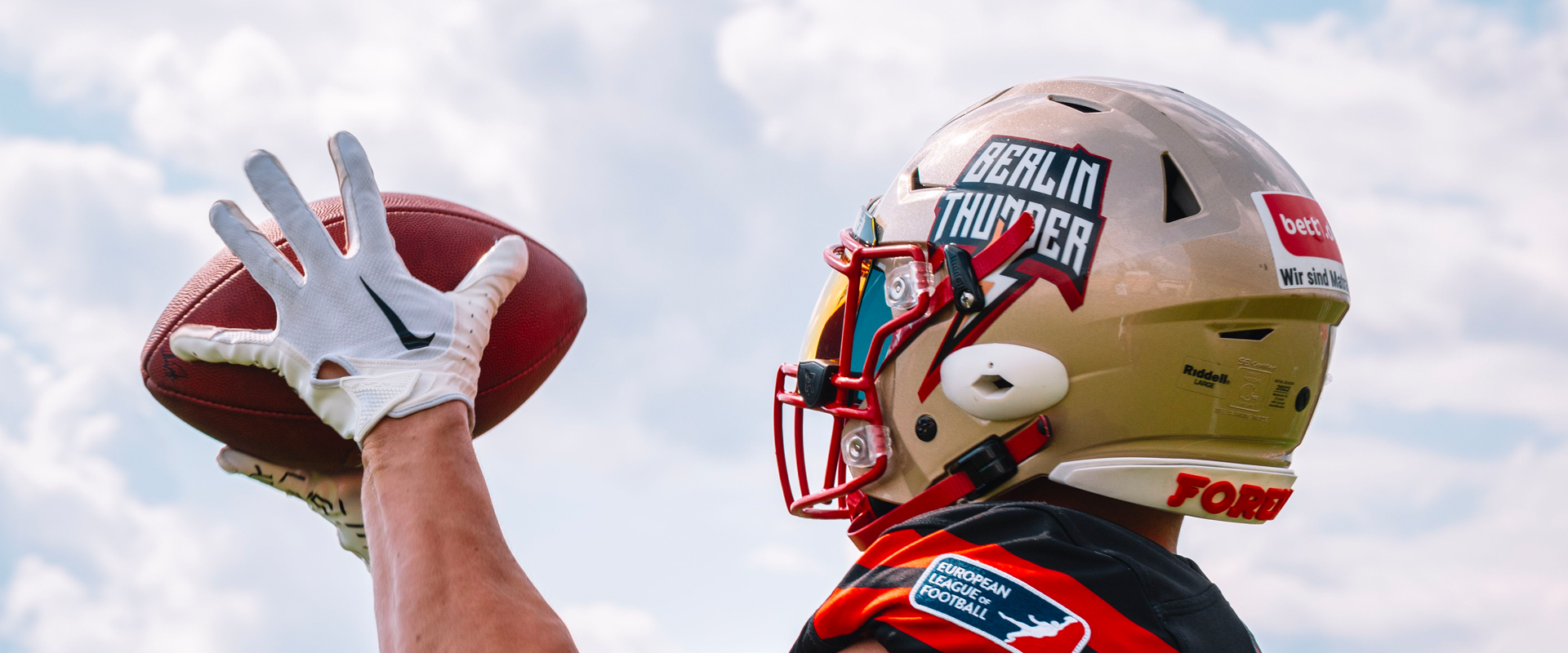 Foto: Eine Person mit Footballhelm und Football in den Händen von hinten.