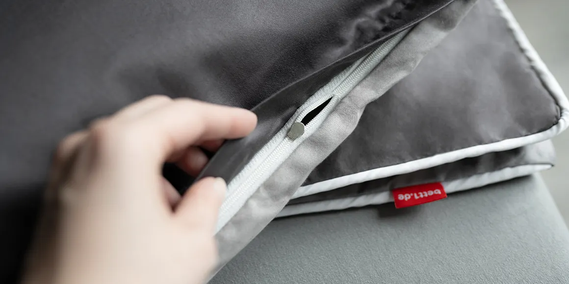 Foto: Eine Hand hält die zusammengelegte SOFT BREEZE Satin Bettwäsche so, dass der Reißverschluss sichtbar ist.