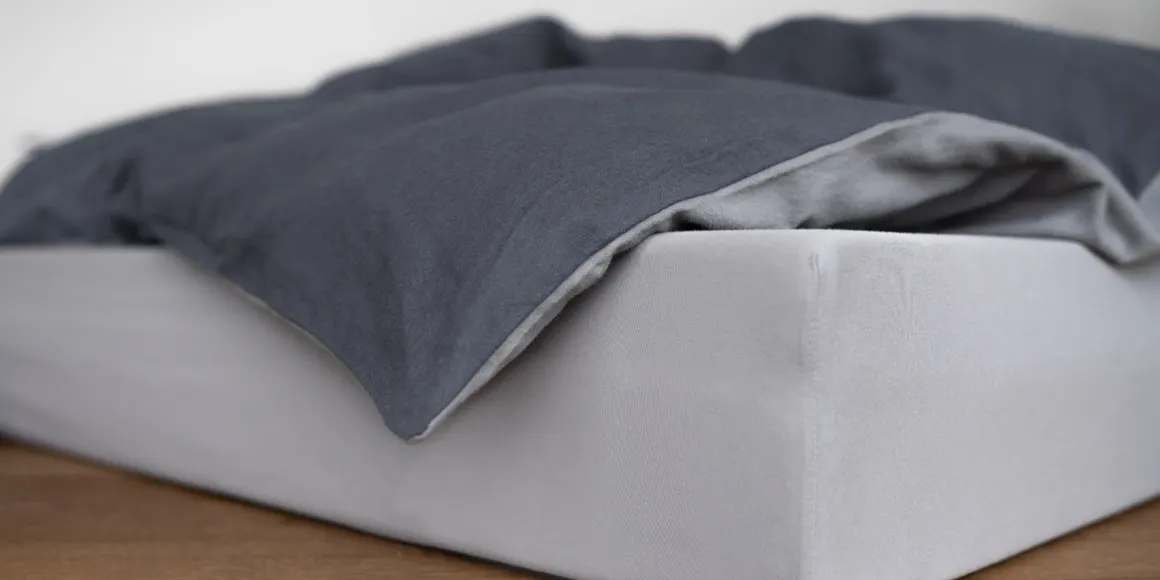 Drap-housse bien tendu sur un matelas, avec une couette gris foncé partiellement repliée.