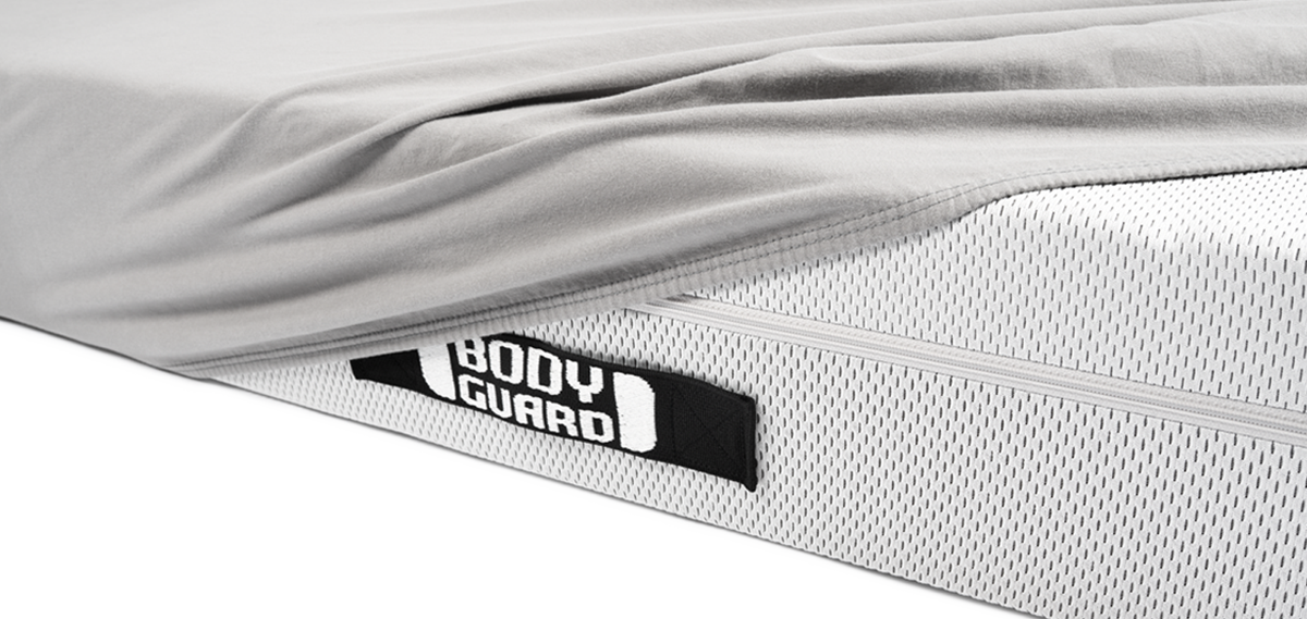 Gros plan sur le côté du matelas BODYGUARD®, recouvert d’un drap gris. La anse noire BODYGUARD est bien visible