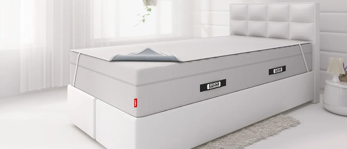 Ein Boxspringbett, auf dessen hoher Matratze eine Inkontinenzauflage gespannt ist.