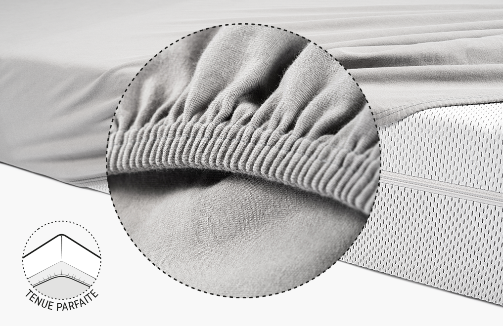 La moitié du matelas BODYGUARD® est recouverte du drap-housse en jersey gris. Zoom sur l'ourlet renforcé et élastique. Illustration montrant le dessous du matelas sur lequel l'ourlet du drap est tiré. Texte : Tenue parfaite
