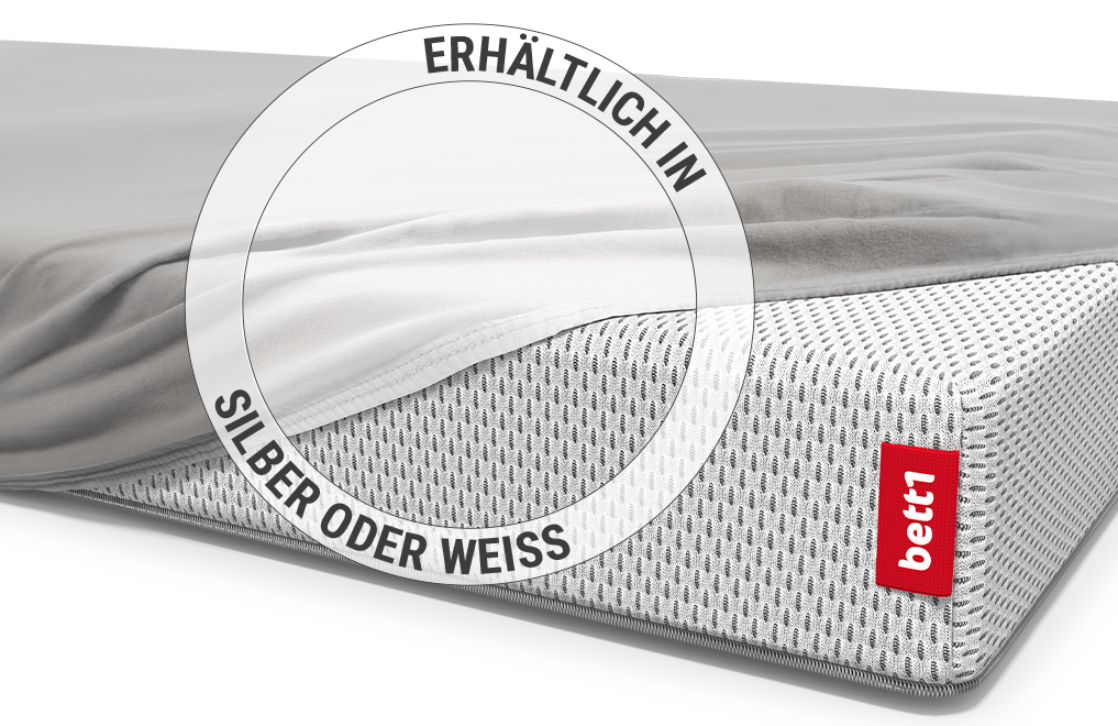 Ein Baby liegt in einem Kinderbett auf einer Babymatratze, die mit dem Kinder-Spannbettlaken in Silber bezogen ist.