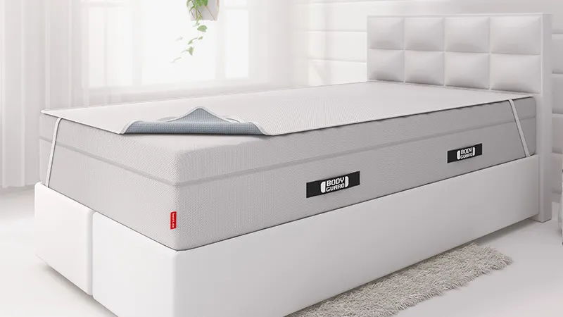 Alèse BODYGUARD® fixé sur un matelas BODYGUARD® à l’aide de sangles élastiques, dans une chambre lumineuse.
