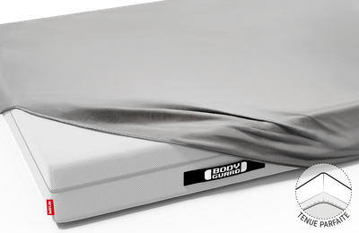 La moitié du matelas BODYGUARD® est recouverte du drap-housse en jersey gris. On voit les poignées noires du Matelas cousues de Bodyguard
