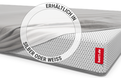 Ein Baby liegt in einem Kinderbett auf einer Babymatratze, die mit dem Kinder-Spannbettlaken in Silber bezogen ist.