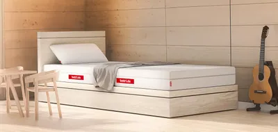 Matelas BODYGUARD® sur un lit en bois clair dans une chambre cosy avec guitare et coin repas.