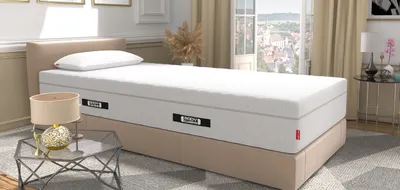 Matelas BODYGUARD® posé sur un sommier tapissier beige dans une chambre élégante avec vue sur la ville.